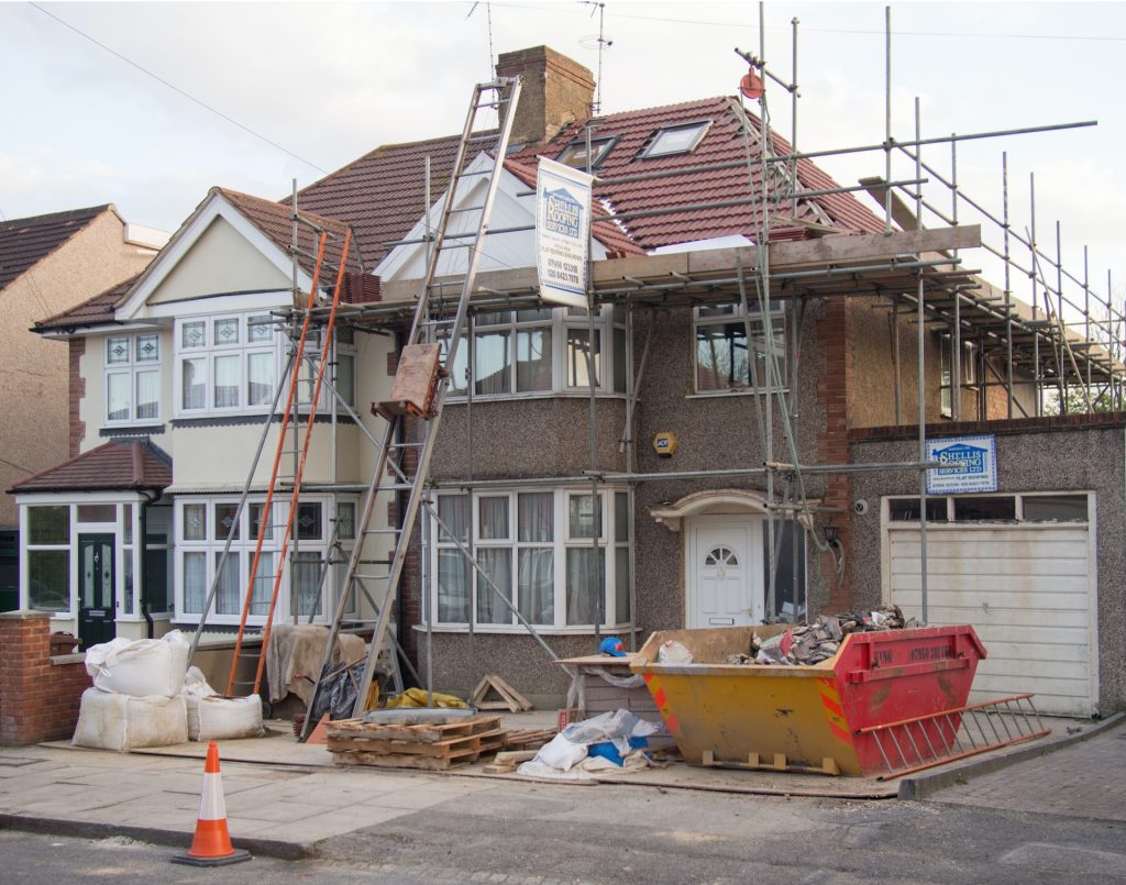 A house with scaffolding and a skip in the garden having some building work